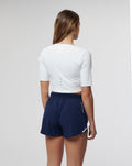 Back view of white cropped Active Contour Top with three back ventilation eyelets worn with navy shorts