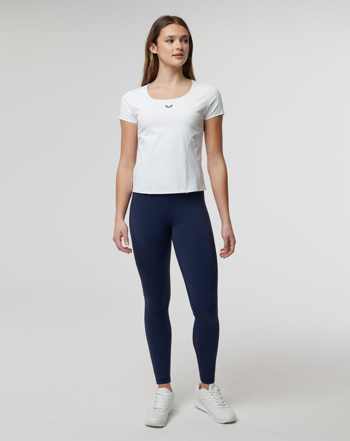 Front view of a woman wearing a white Active Contour Tee, navy leggings and white sneakers.