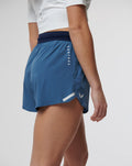 Side view of a model wearing blue Speed Shorts with navy waistband and Castore branding along the side