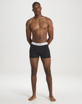 Male model wearing black Castore boxer briefs with white elastic waistband standing against a neutral backdrop.