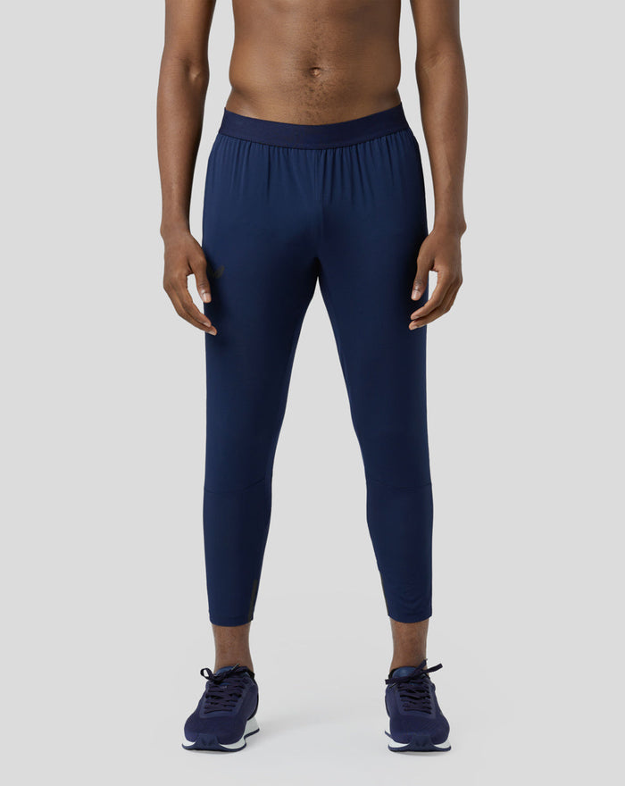 Front view of a model wearing navy Pace Trousers with an elastic waistband and running shoes.