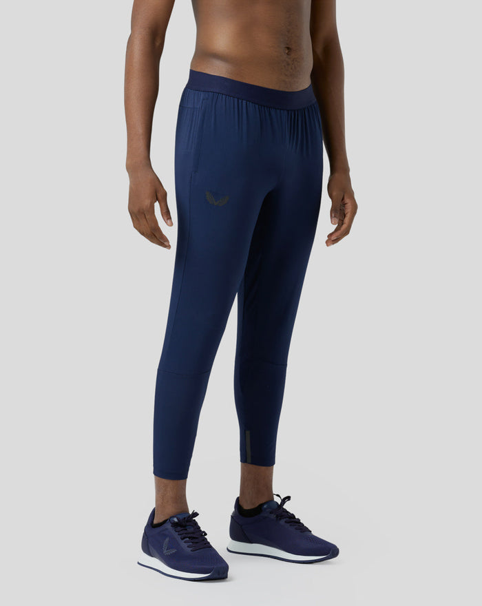Full-length side view of a male model wearing navy Pace Trousers with elastic waistband and running shoes