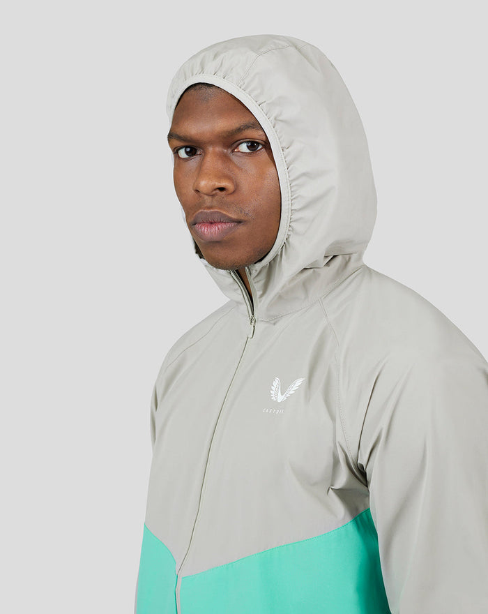 Close-up of a man in a light grey Flyweight Jacket with hood and turquoise lower panel.