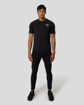 Full-body shot of a male model wearing a black short sleeve training T shirt with a slim fit and a white chest logo.