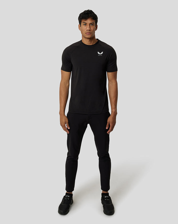 Full-body shot of a male model wearing a black short sleeve training T shirt with a slim fit and a white chest logo.