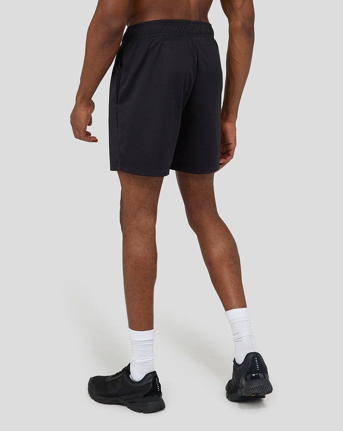Back view of black 6 inch knitted shorts with a small white logo on the left leg, model wearing white socks and black sneakers.