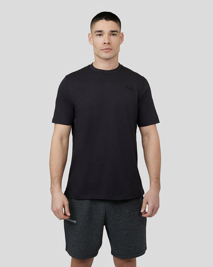 Man wearing a black T-shirt with embroidered Castore logo on chest.