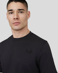 Close-up of a black T shirt showing an embroidered winged logo on the left chest.