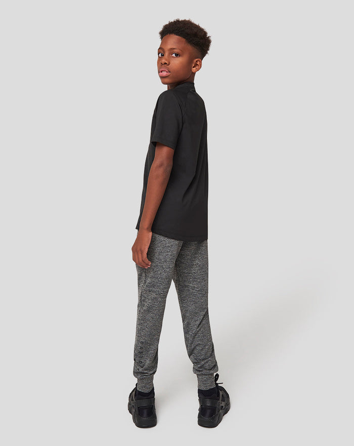 Side view of a young boy in a black t shirt and grey marl joggers against a light gray background