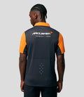 Back view of a man wearing a navy McLaren Formula 1 polo with orange sleeves and collar and team logo on the back