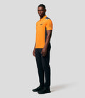 Front view of a male model in a bright orange McLaren replica polo with sponsor logos on the chest and dark side panels