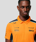 Close up of a man wearing an orange Papaya McLaren polo with navy shoulders and a light blue stripe