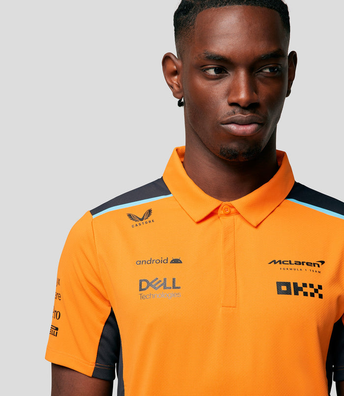 Close up of a man wearing an orange Papaya McLaren polo with navy shoulders and a light blue stripe