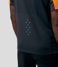 Back view of a model wearing an orange and navy McLaren replica polo with light blue ventilation dots along the lower back
