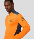 Side view of model in orange McLaren replica quarter zip top with black side panel and sleeve sponsor logos visible.