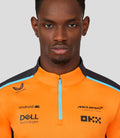 Close-up of a male model wearing an orange McLaren replica quarter zip top with a blue zipper.