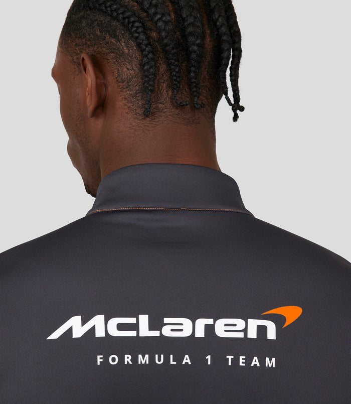 Front view of a male model in an orange McLaren replica quarter zip top with blue zipper and sponsor logos.