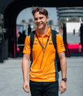 Model wearing a Papaya and Phantom McLaren polo with navy side panels and multiple sponsor logos on the chest.