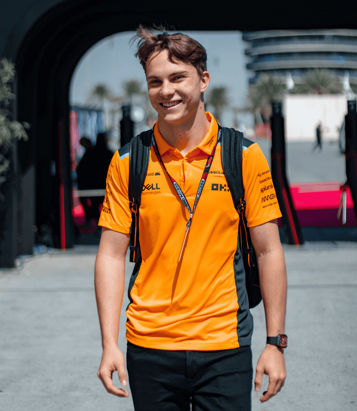Model wearing a Papaya and Phantom McLaren polo with navy side panels and multiple sponsor logos on the chest.